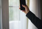 Close-up of a hand holding a smartphone by a window